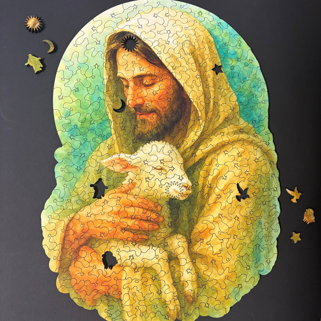 Jigsaw puzzle of a watercolor-style illustration of Jesus Christ wearing a hooded robe, gently holding a small white lamb in His arms. Both have peaceful, closed eyes, conveying tenderness and protection. The background is a soft green wash, giving the image a calm, serene feeling.